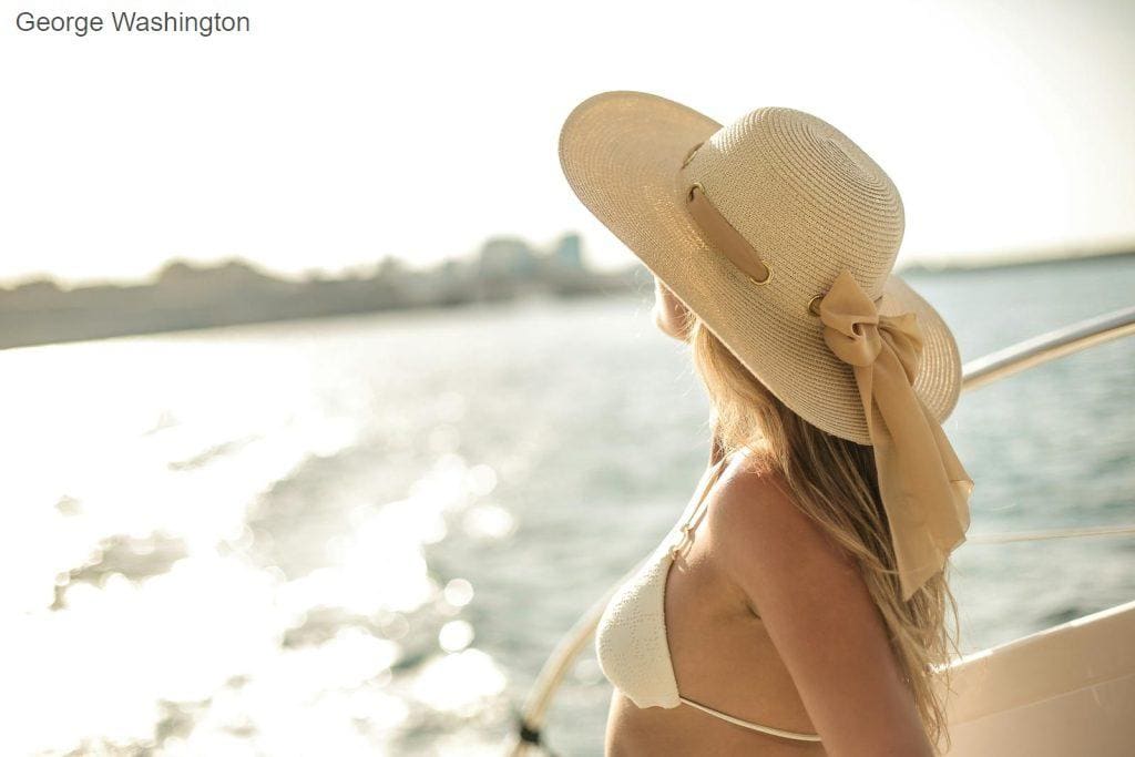 Back view of slim female in bikini top and straw hat enjoying trip on cruise boat on sunny day while relaxing during summer vacation and looking away